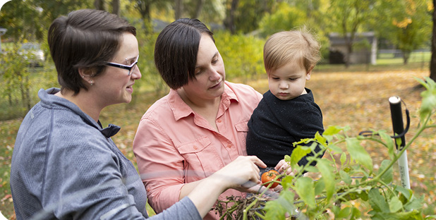 Mom's show their toddler son some plants in the garden.